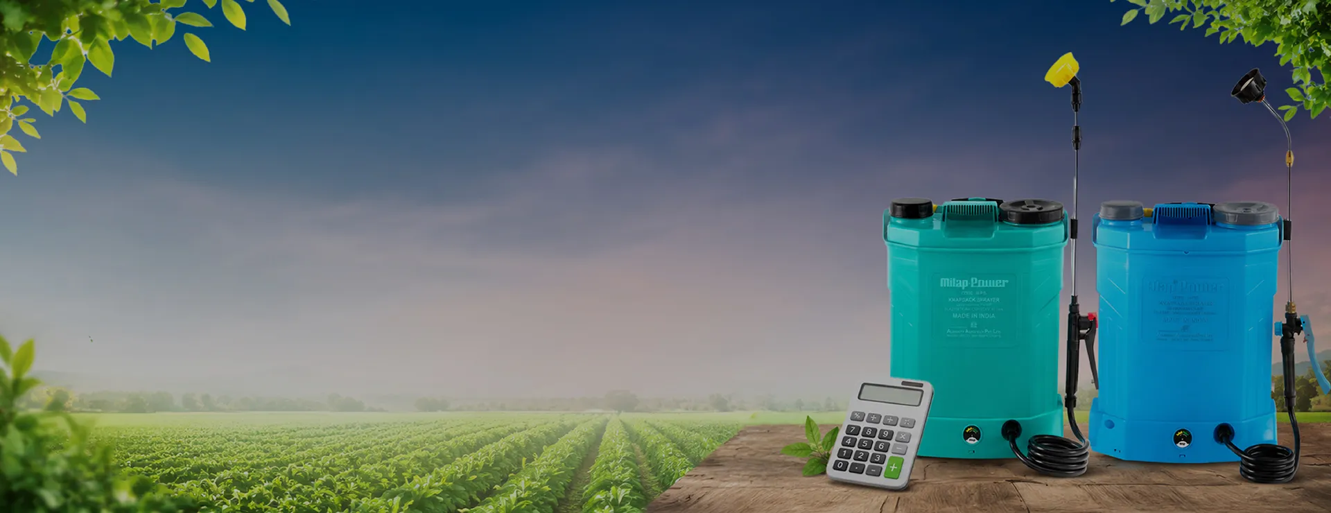 Two ALAP knapsack battery sprayers and a calculator on a table beside a crop field